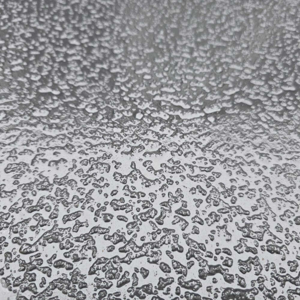 Rain droplets forming textured patterns on a black metal surface with tonal bands and squared-off illusion.