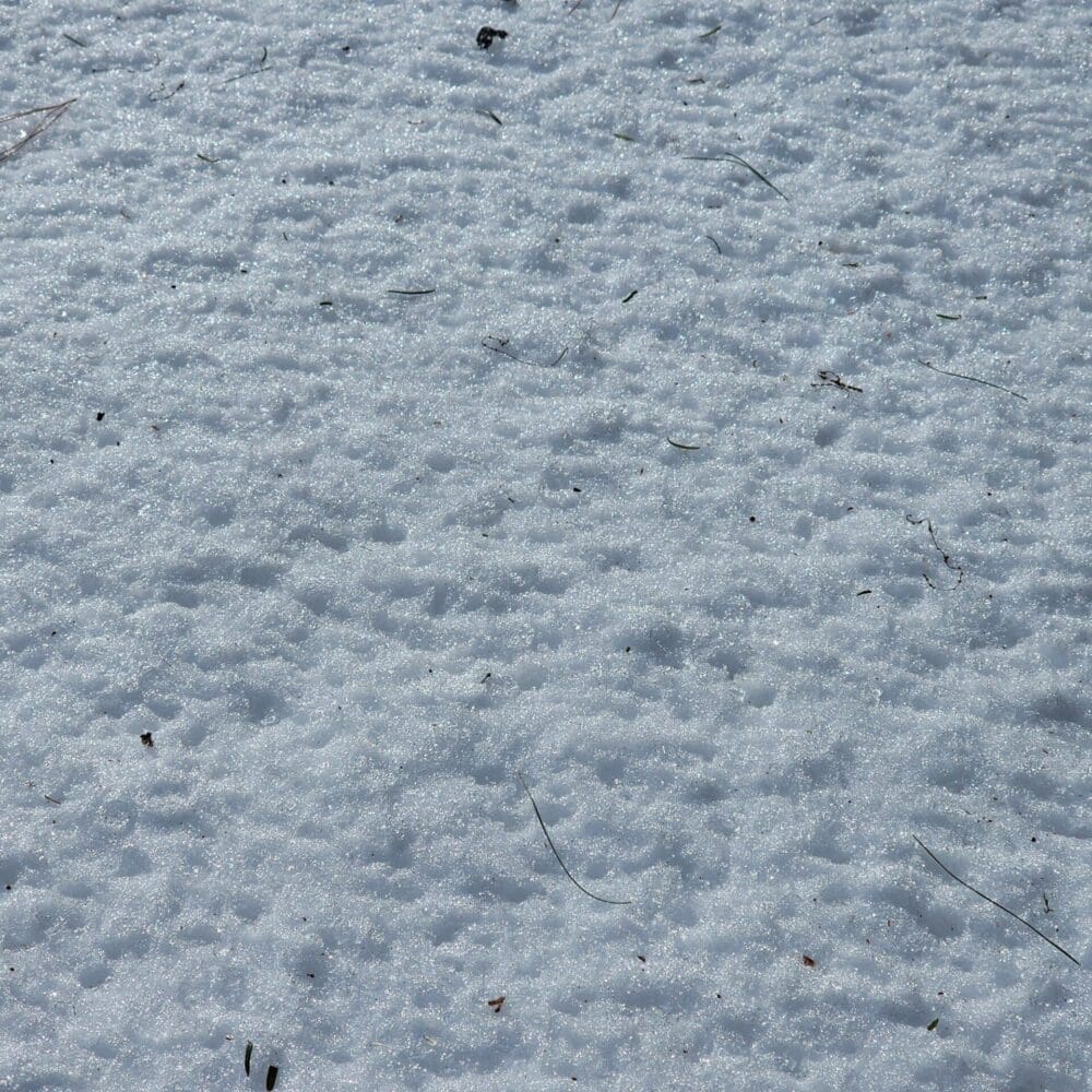 Close-up of snowy surface with tiny dimples and spikes, resembling white sandpaper.