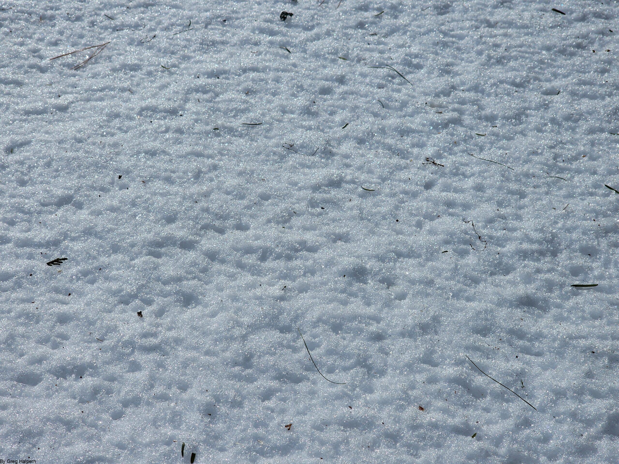Close-up of snowy surface with tiny dimples and spikes, resembling white sandpaper.